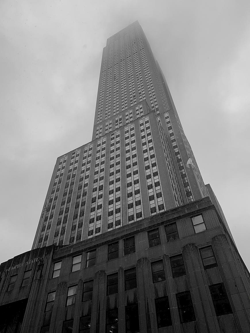 a black and white photo taken from below looking up at a large skyscraper as it lengthens into a cloudy sky