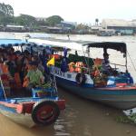 A group of 25 students on a large boat in a water-based marketplace.