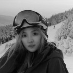 A person with a ski helmet and goggles on top of their head with a ski slope in the background.