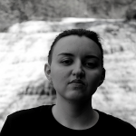 A person wearing a black shirt standing in front of a waterfall.