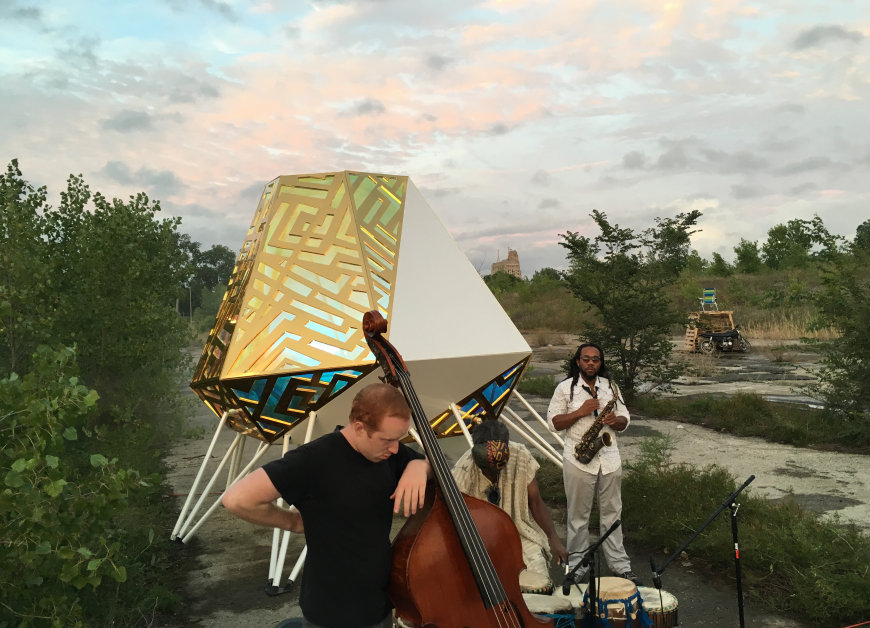 A person holding a cello next to a large spacecraft and a person holding a saxophone. 