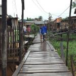 students walk on a raised walkway between informal housing built on stilts