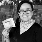 A smiling person with glasses holding a small paper.
